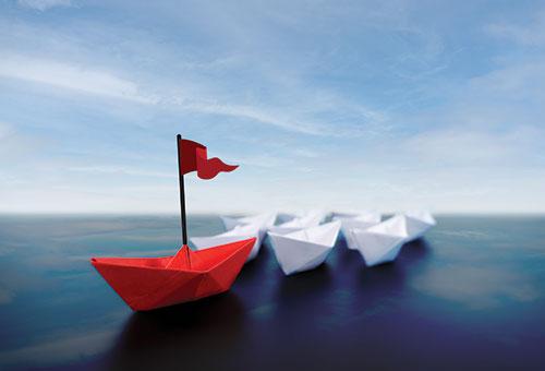 a flotilla of paper boats with a red boat with a flag leading