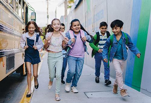 young students running next to a school bus