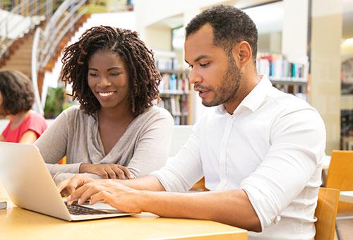 a man and a woman writing on a laptop at a library