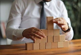 Businessman hand pulling out or placing wood block on the tower and semi pyramid in modern office. plan and strategy in business.